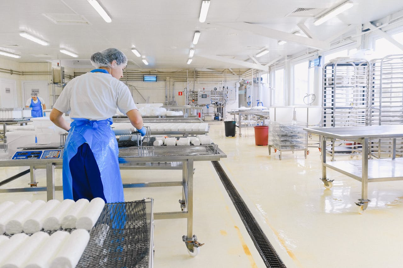 A worker in protective gear handles cheese in a modern dairy factory setting.